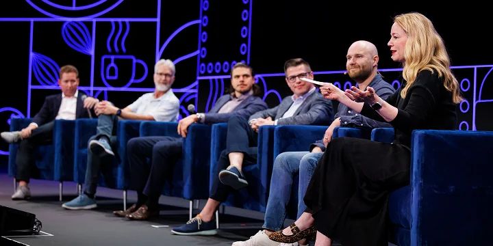 A panel of speakers sitting on stage with a large audience backdrop.