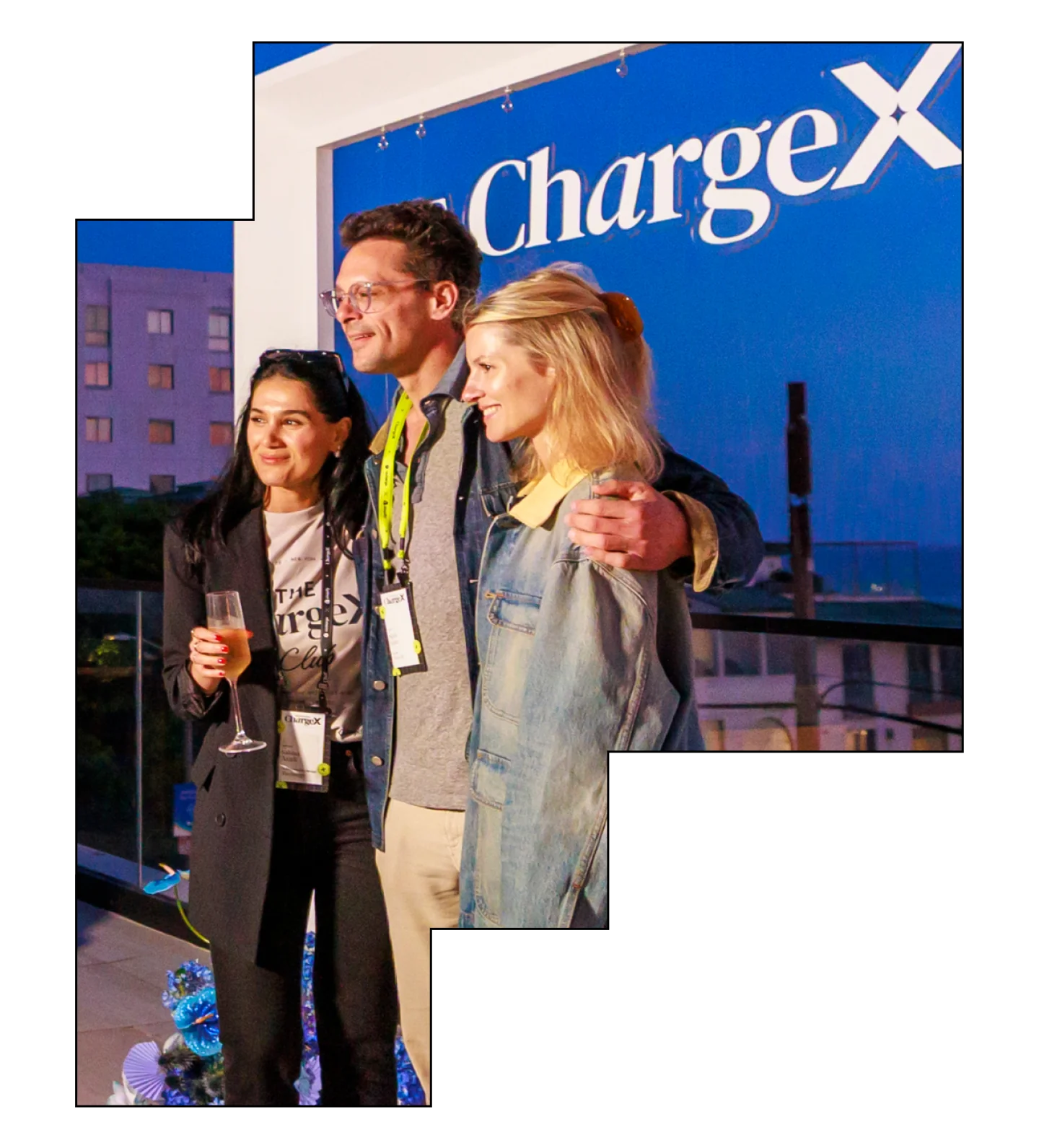 Three people pose together at an event with a ChargeX banner in the background.