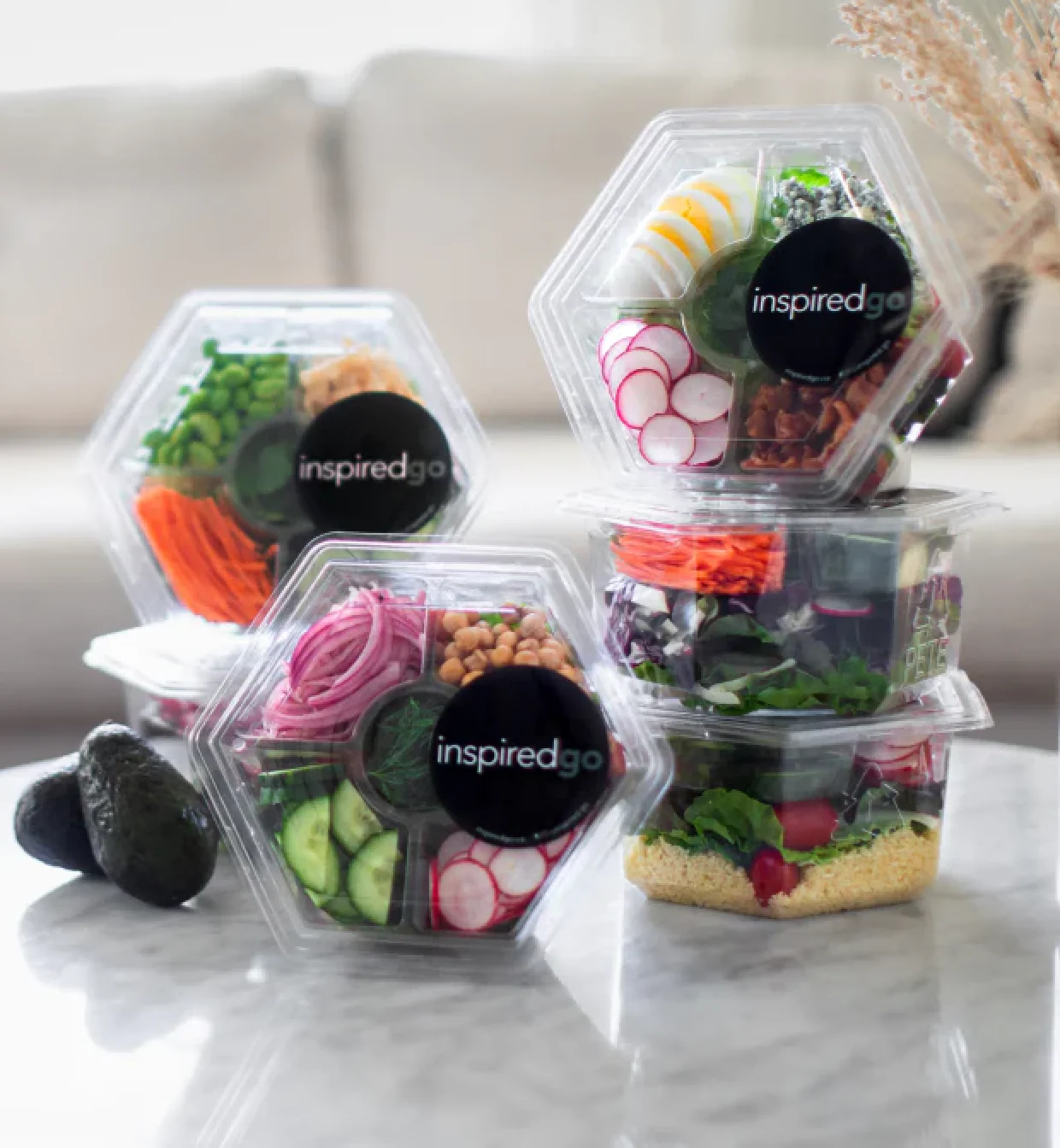 Four Inspired Go salad containers filled with various vegetables.