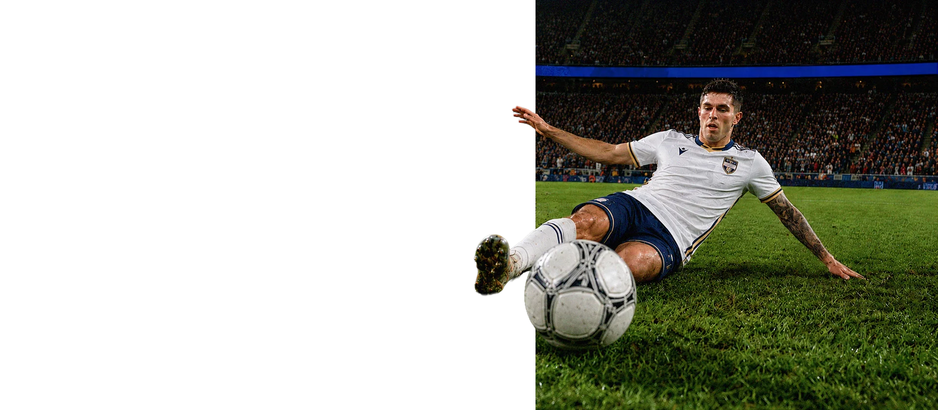 A soccer player sliding on the grass field while attempting to control the ball during a match.