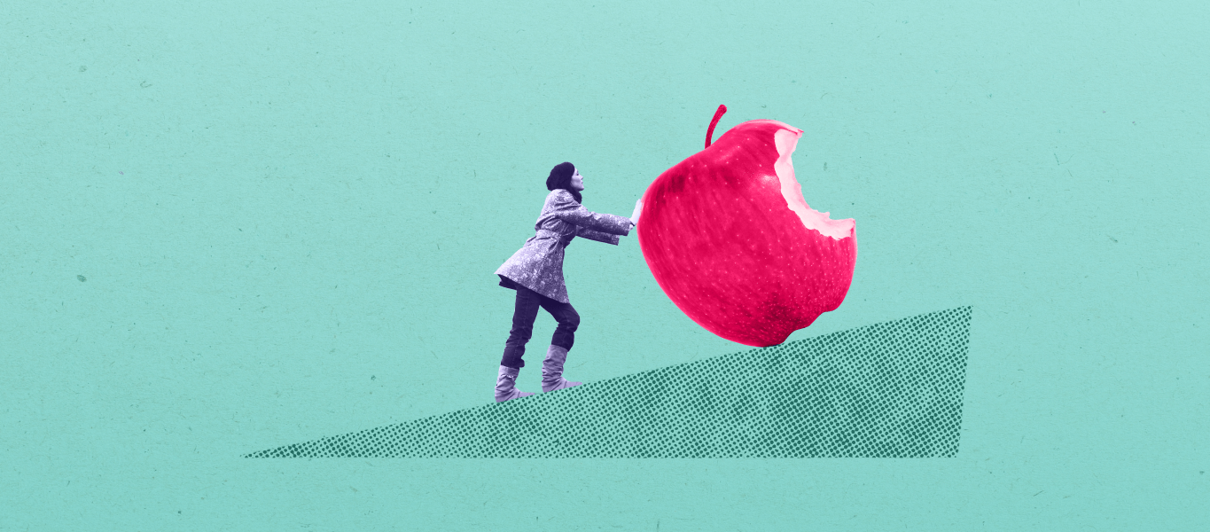 Person pushing a giant apple, with a bite taken out of it, up a slope