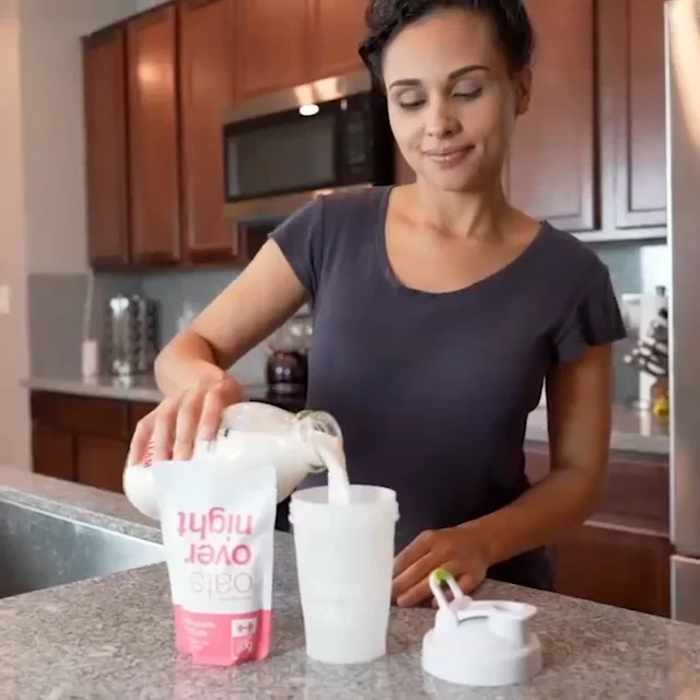 A person pours milk from a container into a cup on a kitchen countertop.