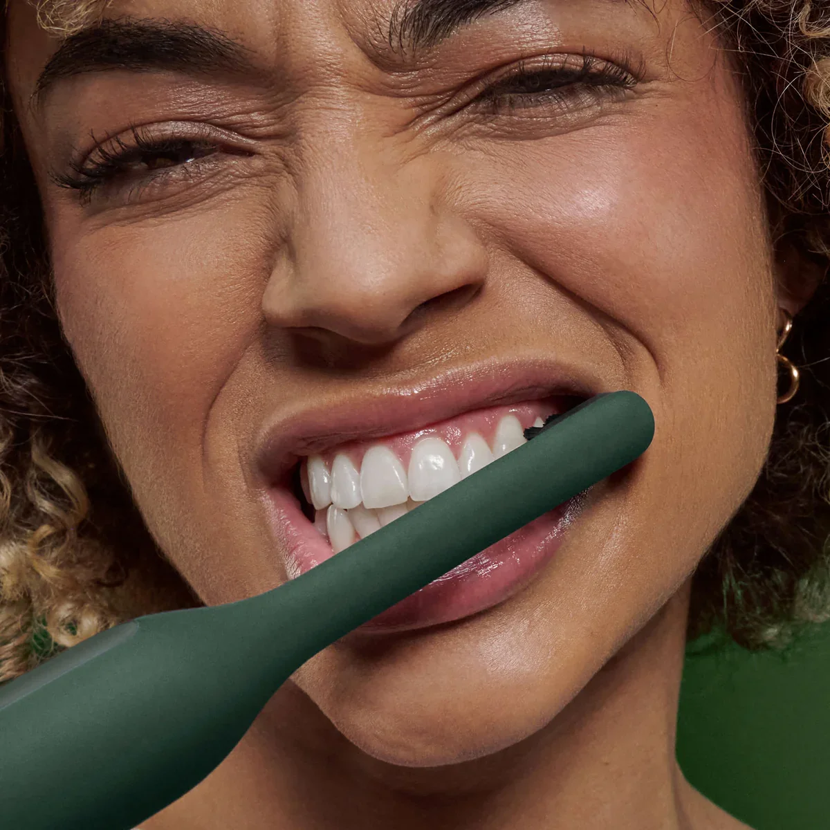 A person brushing their teeth with a green toothbrush.