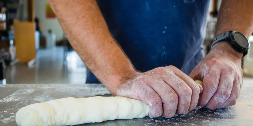 A person rolling dough on a kitchen countertop.