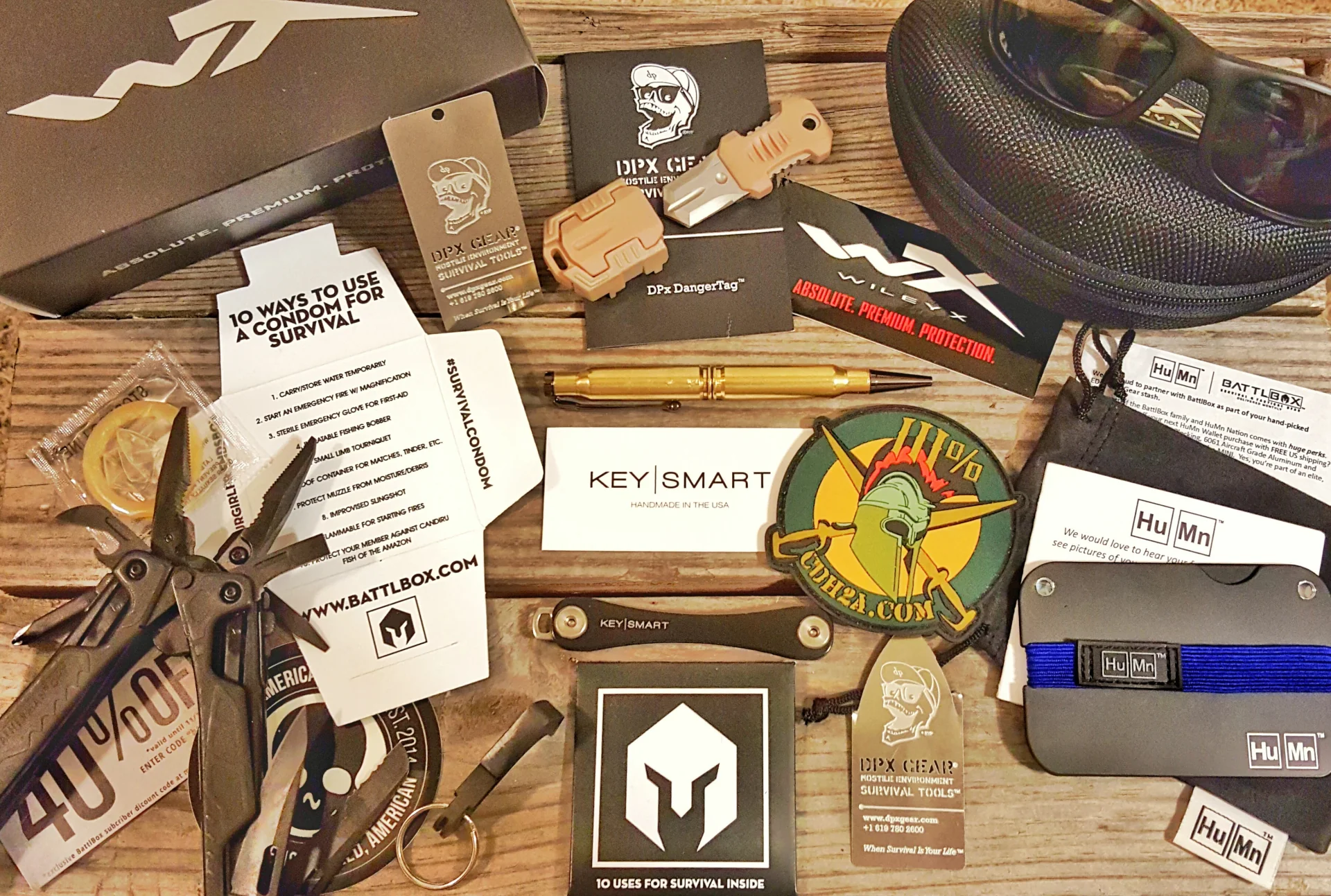 An assortment of survival tools and promotional materials from BattlBox and related brands on a wooden table.