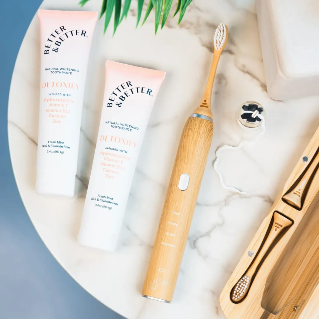 Two tubes of Better & Better toothpaste and an electric toothbrush on a marble surface.