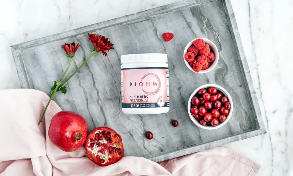 BIOHM Super Reds product positioned on a marble tray with raspberries and pomegranate.