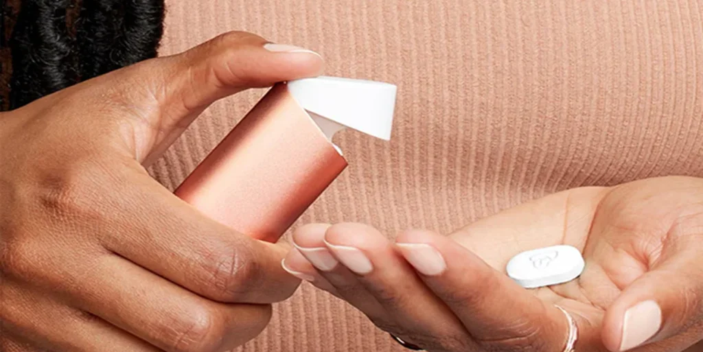 A person holding a pearlescent quip dispenser and a small tablet in their hand.