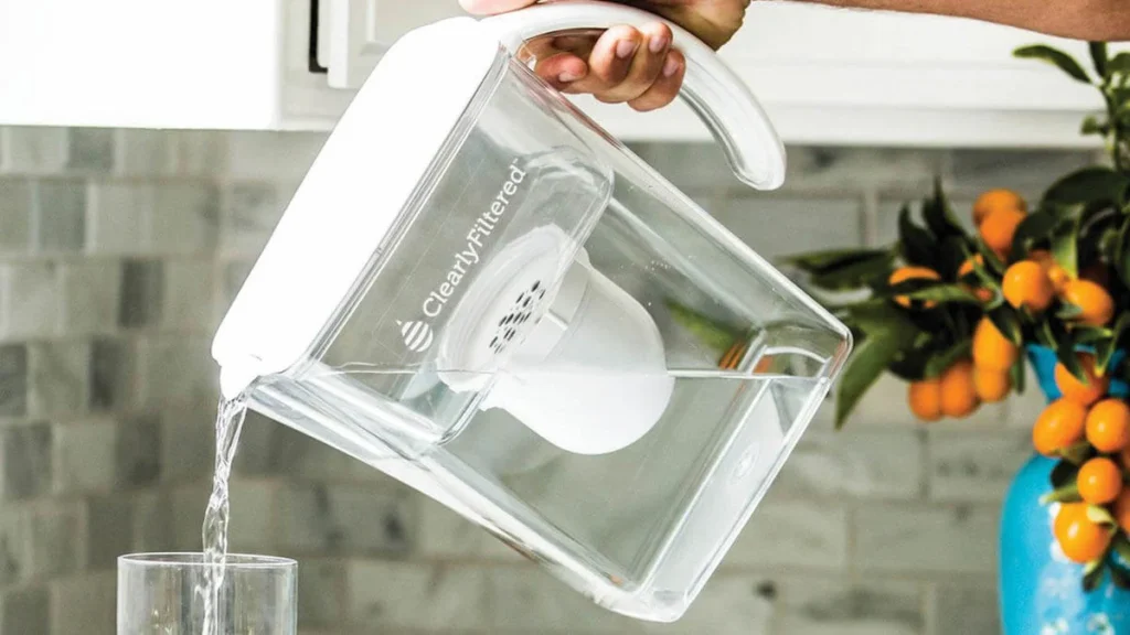 A person pouring water from a ClearlyFiltered pitcher into a glass.