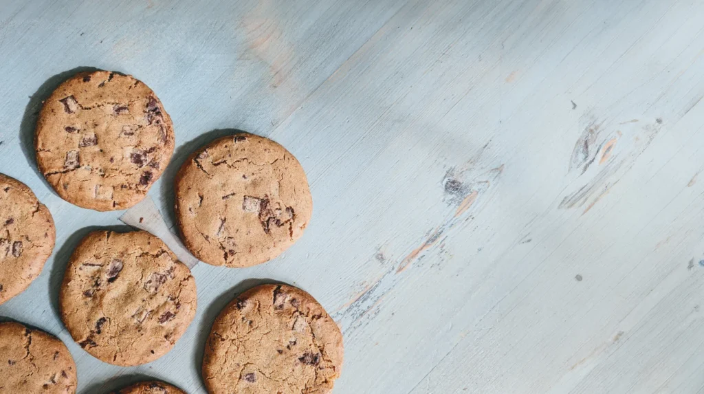 Several chocolate chip cookies on a light blue wooden surface.