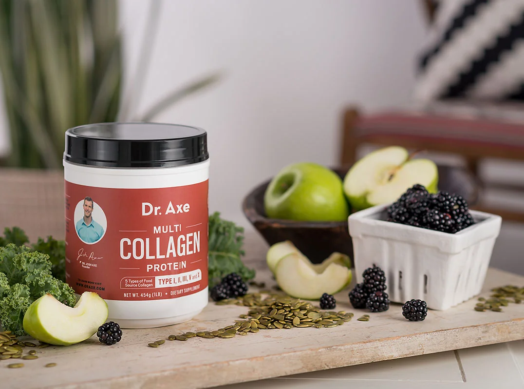 A container of Dr. Axe Multi Collagen Protein surrounded by fruits and vegetables on a wooden surface.