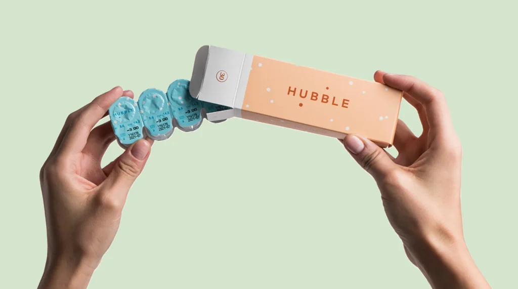 A person's hand holding a Hubble contact lens packaging with lenses visible inside.
