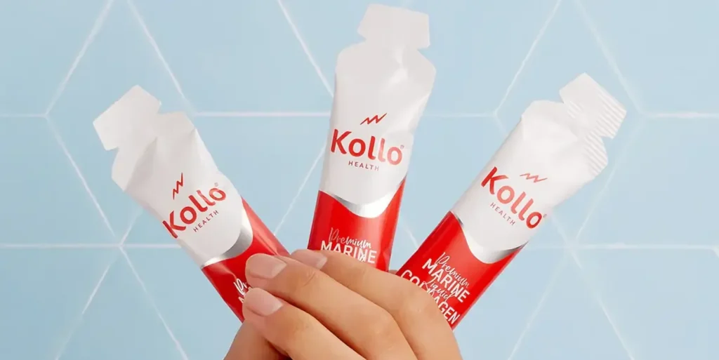 A hand holding three Kollo Health product packs against a light blue background.