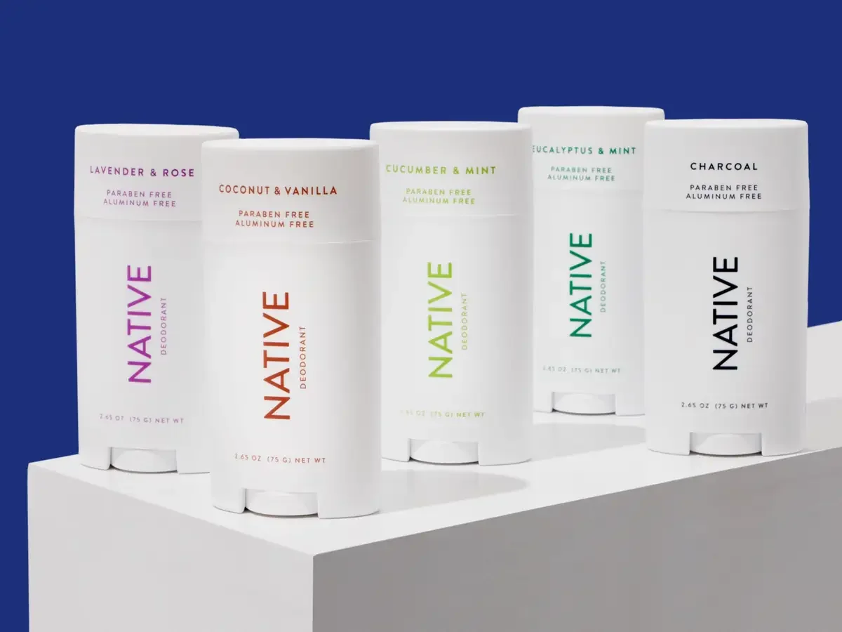 Five Native Deodorant sticks in different scents placed on a white surface against a blue background.