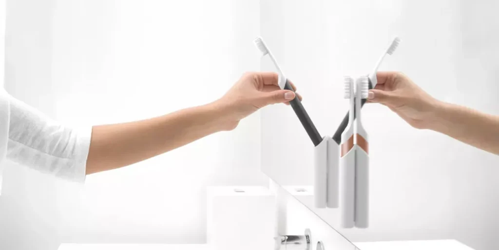 A mirror reflecting two toothbrushes being placed on a bathroom counter.