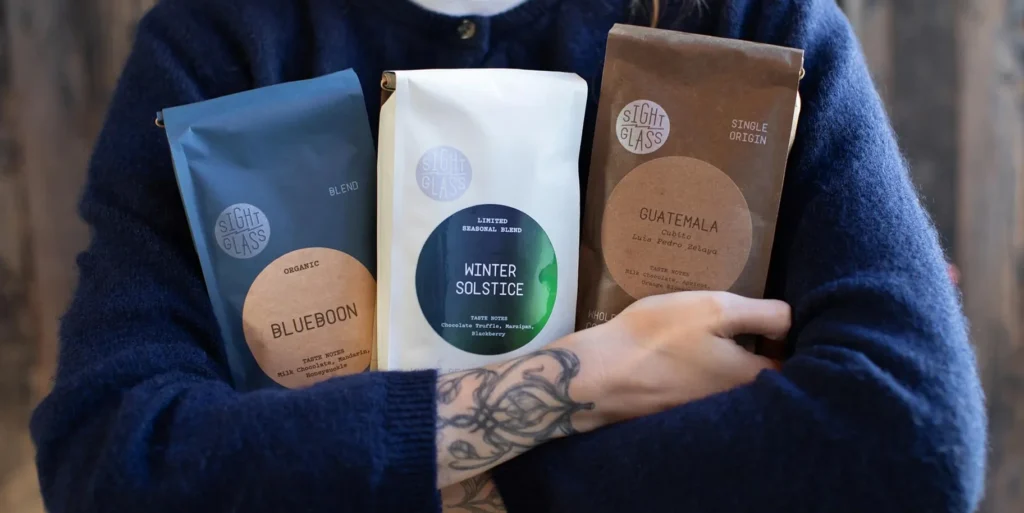 A person holding three coffee bags from Sight Glass.
