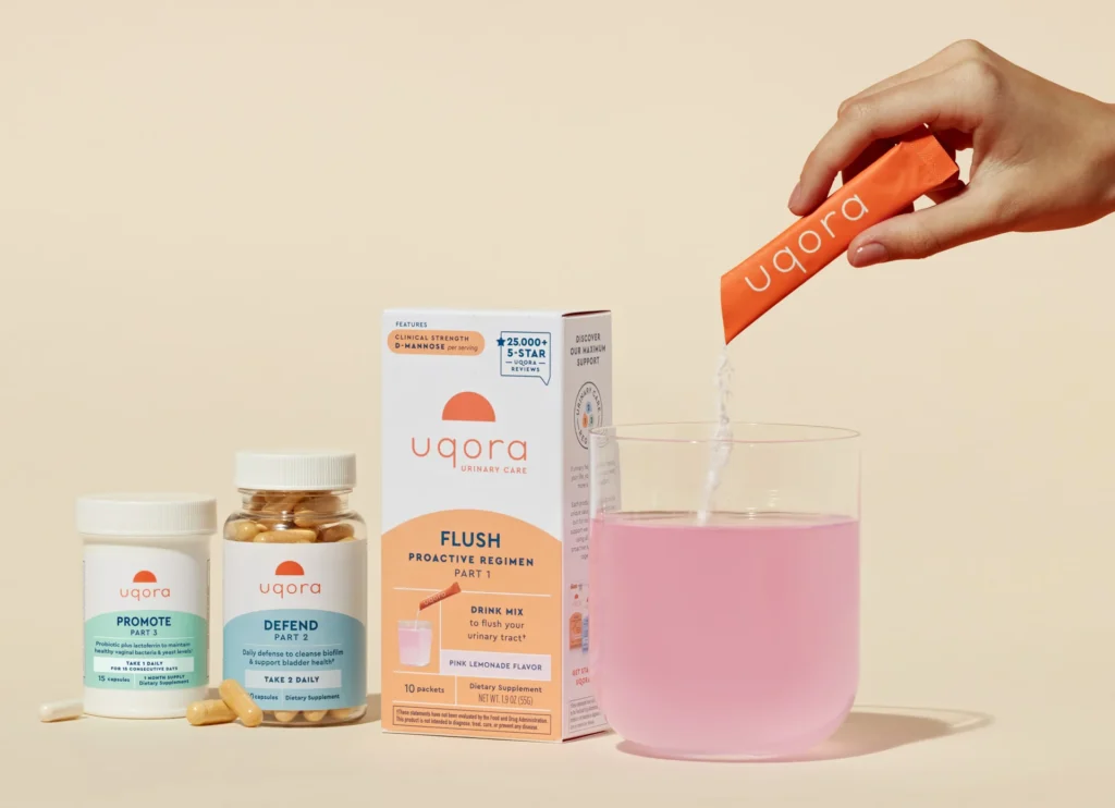 A hand pouring Uqora Flush drink mix into a glass of water, creating a pink beverage.