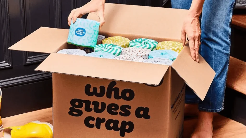 A person opening a box full of colorful toilet paper rolls labeled with Who Gives A Crap.