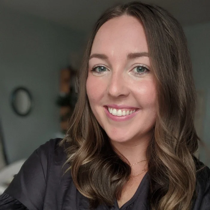 A woman with long hair smiling at the camera in a softly lit room.