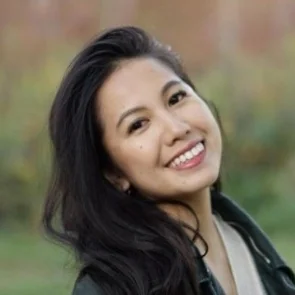 A person smiling outdoors with long dark hair.
