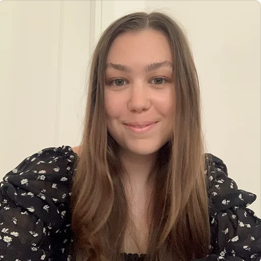 A person smiling and looking at the camera, with long brown hair and wearing a floral black top.