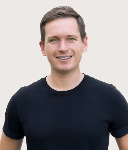 A person smiling and wearing a black t-shirt against a light background.