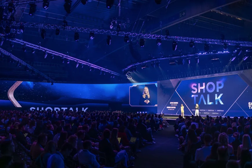 Two speakers on stage during a presentation at the Shoptalk conference.