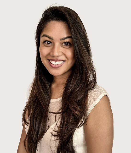 A portrait of a woman smiling with long, dark hair and wearing a light shirt.