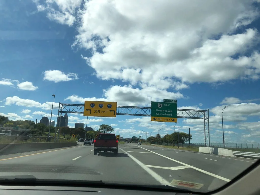 A highway view with traffic signs and clouds in the sky.