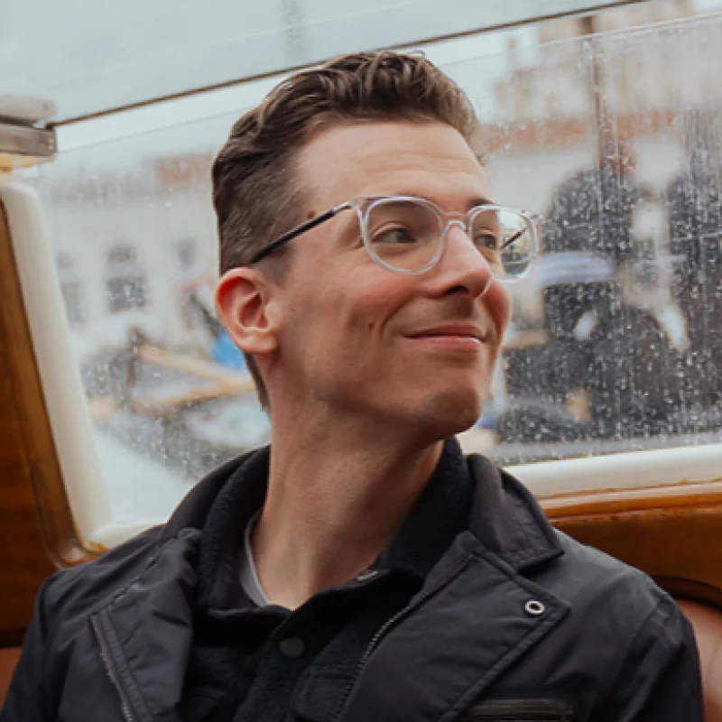 Scott Meiklejohn smiling while sitting in a boat, with rain on the window behind him.