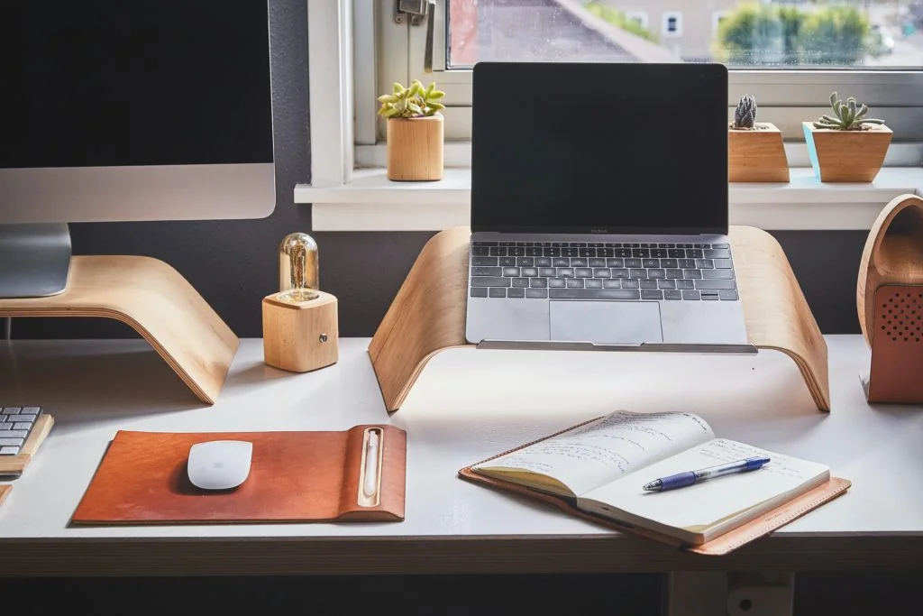 A workspace with a laptop, mouse, notepad, and decorative plants.