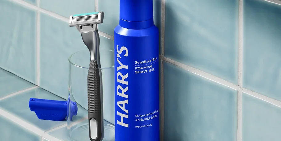Harry's sensitive skin foaming shave gel alongside a razor on a glass surface.