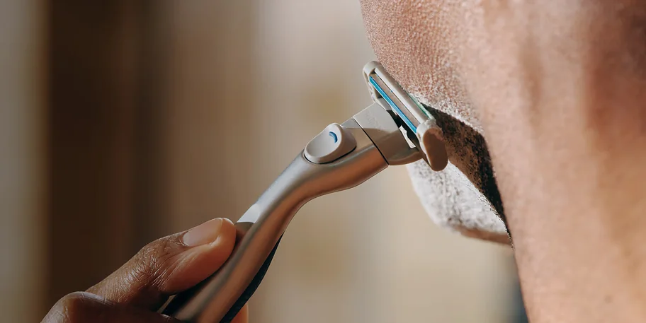 A close-up of a person using a razor on facial hair.