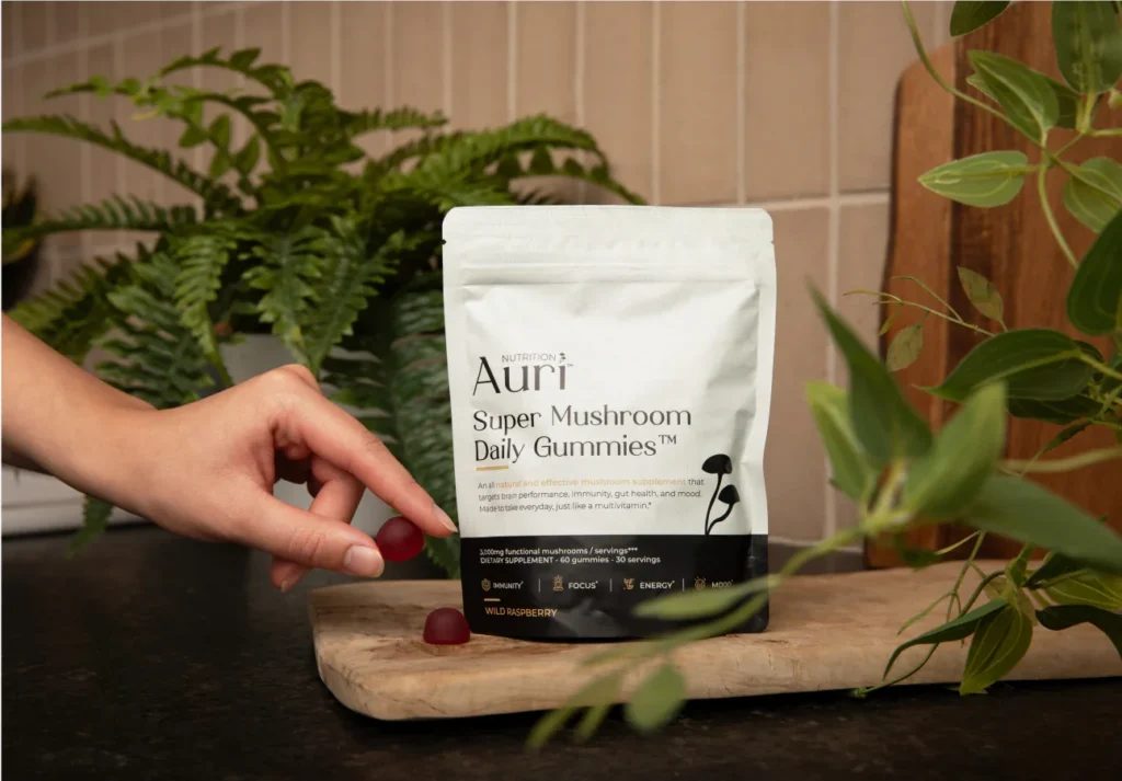 A hand reaching for red gummies beside a bag of Auri Super Mushroom Daily Gummies.
