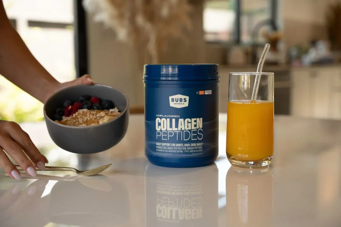 A person holding a bowl of oats with berries next to a container of Bubs Naturals Collagen Peptides and a glass of juice.
