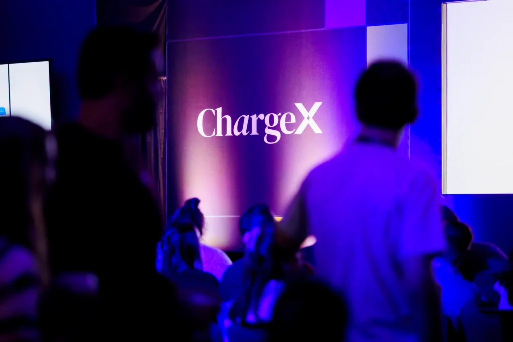 Background display featuring the ChargeX logo at a conference setting.