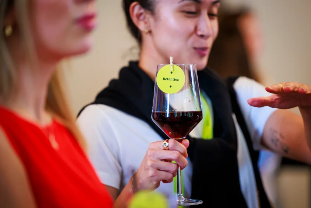 A close-up of a person holding a wine glass with a tag labeled 'Retention'.
