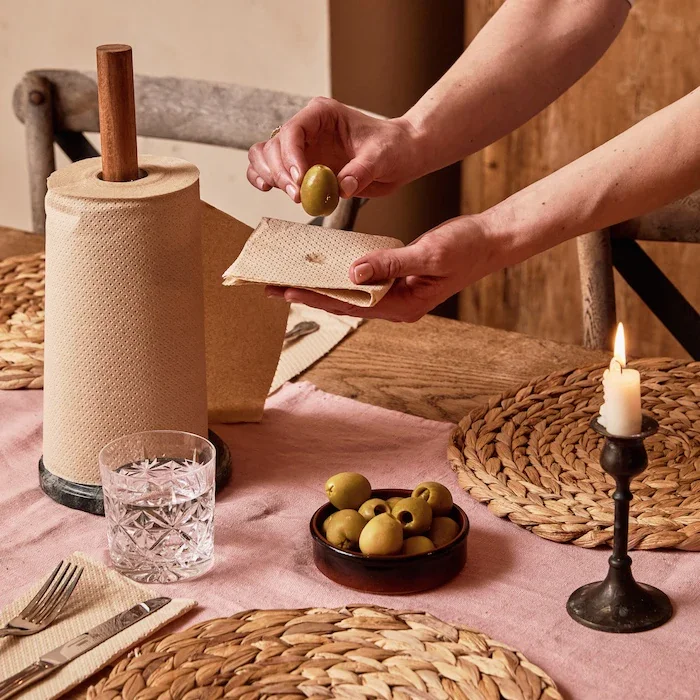 A person placing an olive on a reusable paper towel in a rustic table setting.