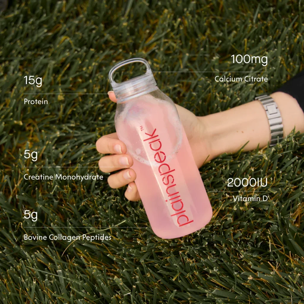 A person holding a nutritional supplement bottle on grass, displaying various nutrient content.