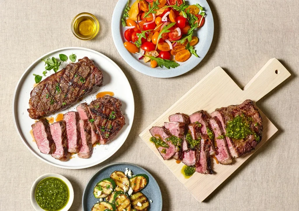 Grilled steak sliced and served with a green sauce alongside a fresh salad with cherry tomatoes and arugula.