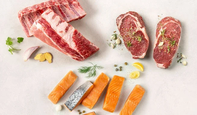 A selection of raw meat and fish including ribs, beef steaks, and salmon.
